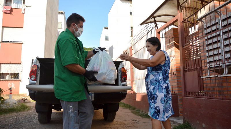 Imagem da entrega de uma cesta básica à uma idosa por um voluntário da CEASA/RS.